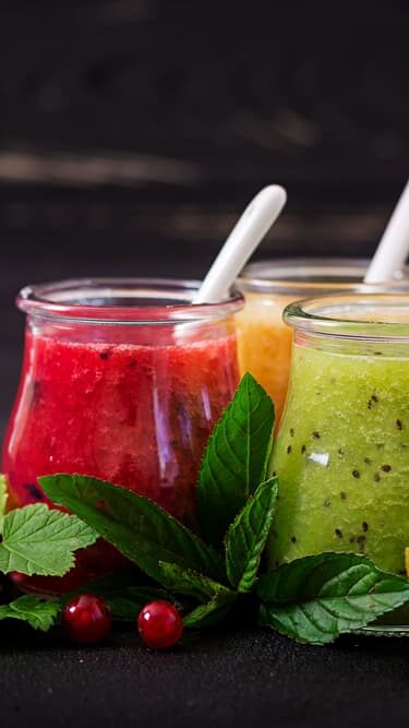 A group of glasses filled with freshly blended fruit juices including watermelon, kiwi fruit, and orange plus herbs in the foreground