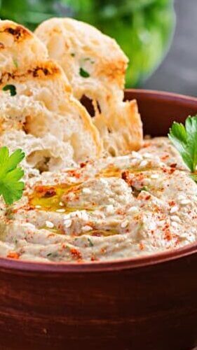 A cropped view of a vegan dish with toasted bread slices on the side in an earthenware bowl